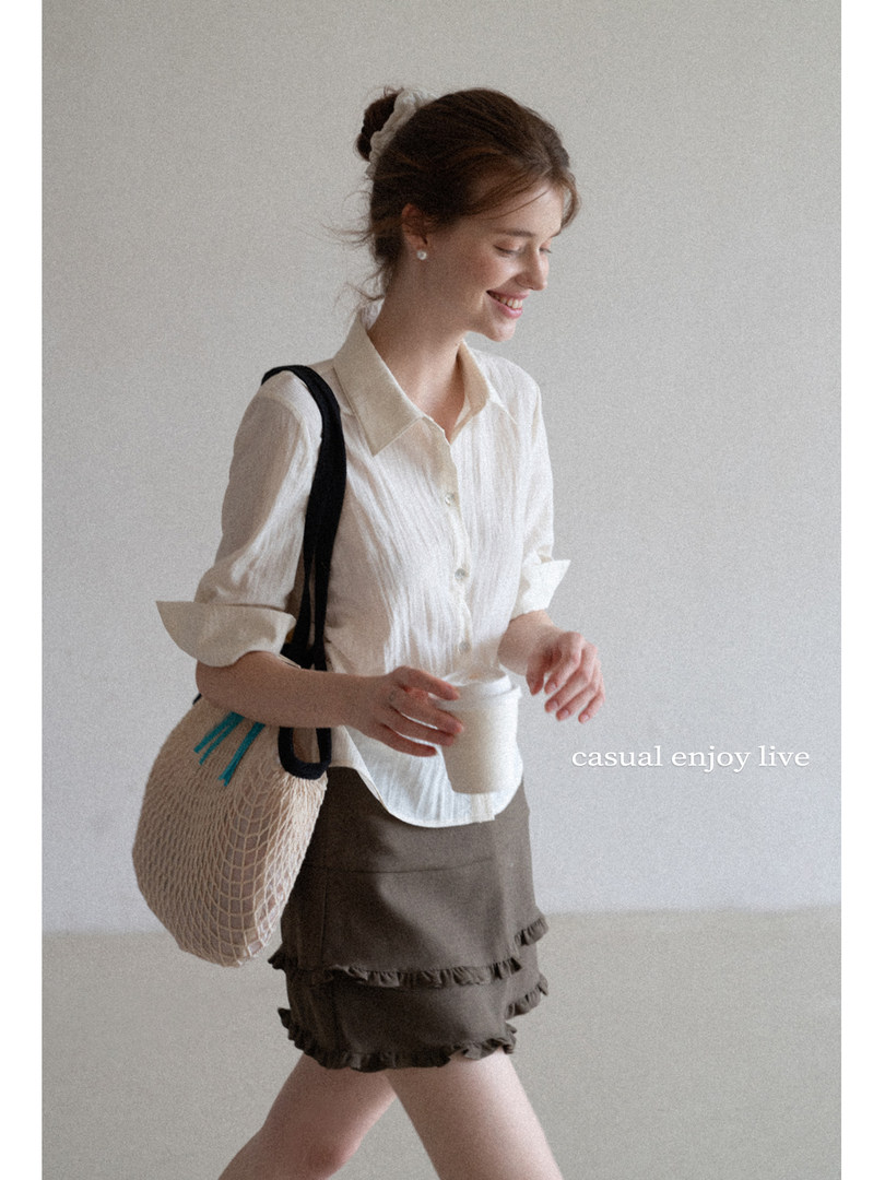 Woman wearing a white blouse and ruffled shorts with a woven shoulder bag