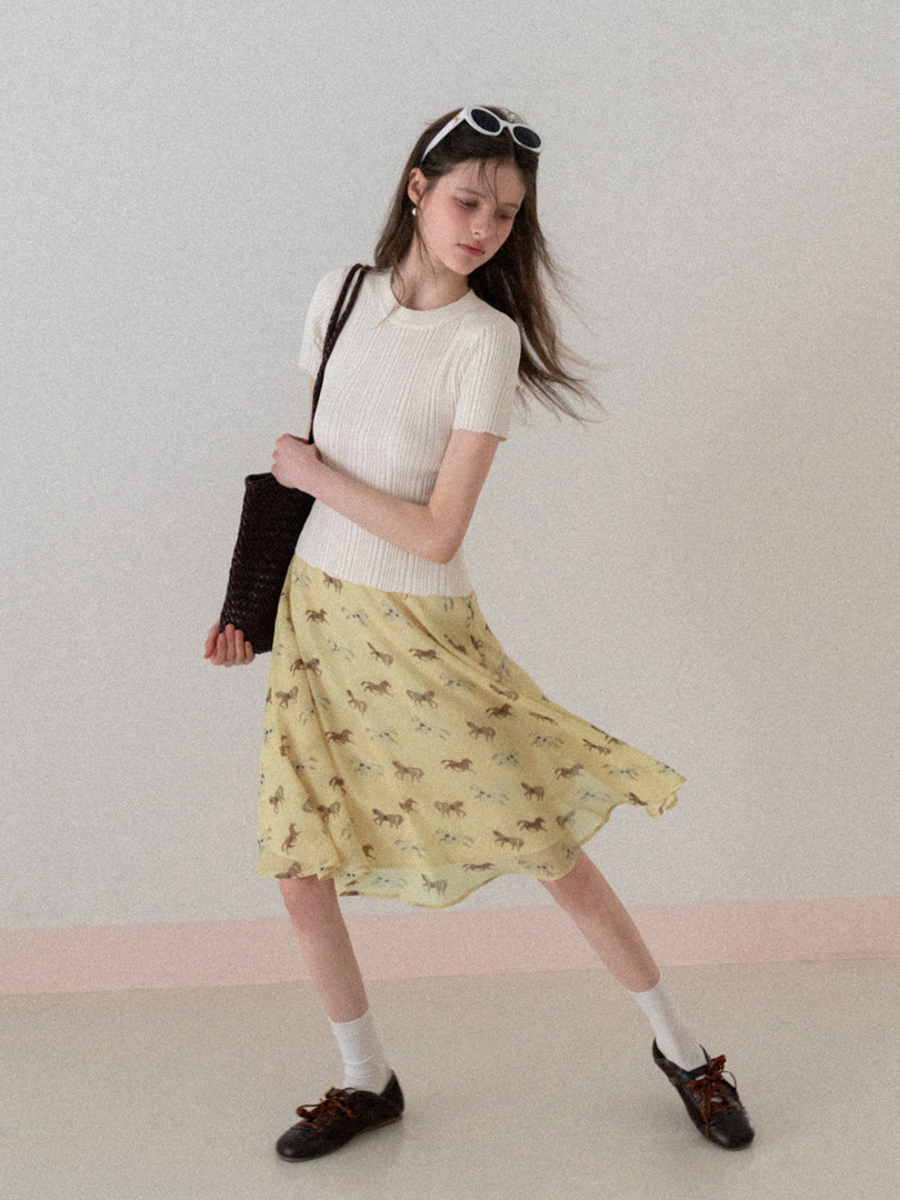 Model wearing a white short-sleeve knit top with a yellow printed midi skirt and black shoes