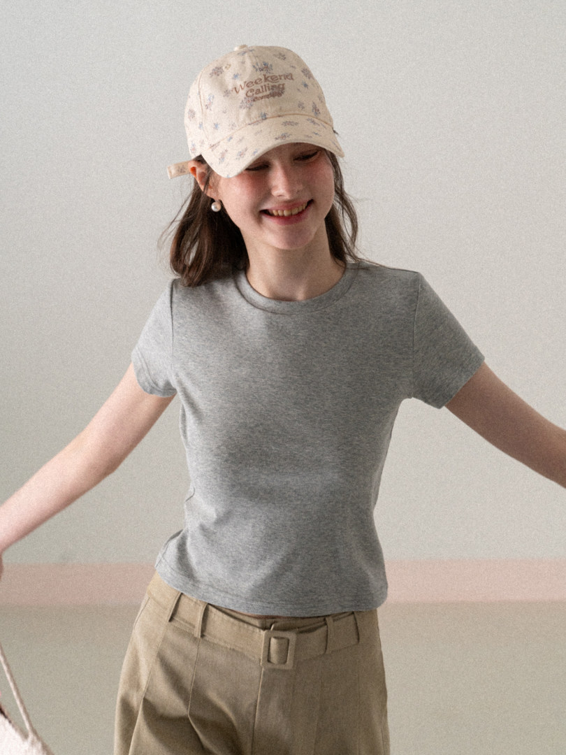Woman wearing a gray fitted t-shirt with a beige printed cap and beige pants