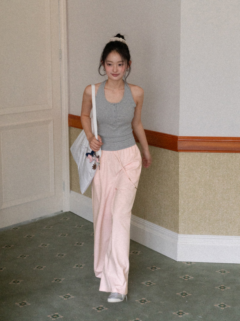 Woman wearing a gray halter tank top with light pink wide-leg pants and a white tote bag