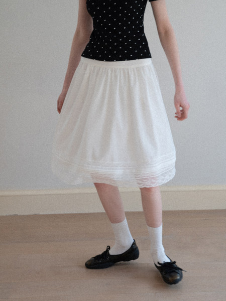 Model wearing a black polka dot top with a white midi skirt and black flats