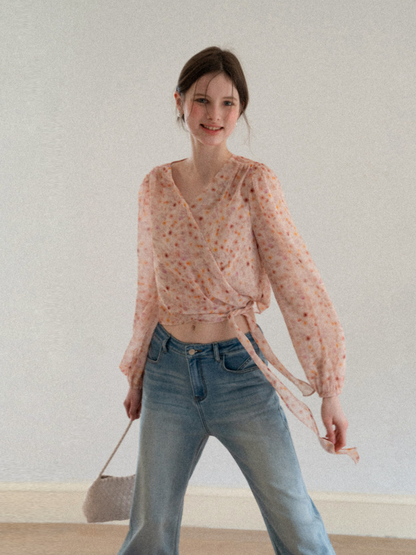 Model wearing a sheer floral wrap blouse with light blue jeans