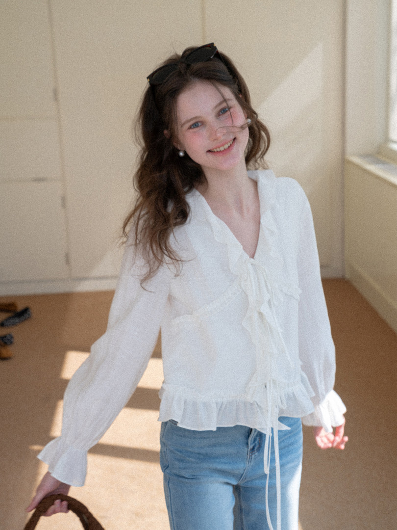 Woman wearing a white sheer long-sleeve blouse with tie detail and light blue jeans
