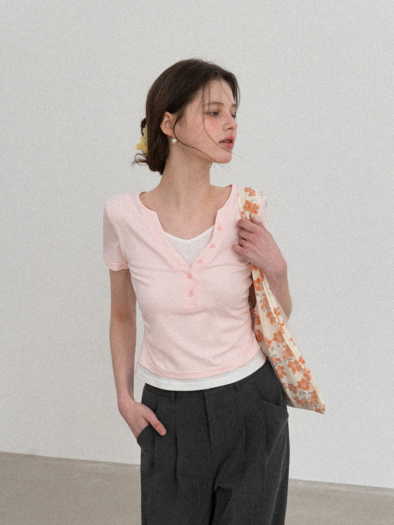 Model wearing a light pink short-sleeve button-front top with a floral tote bag
