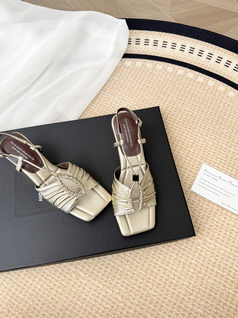 Pair of gold strappy heeled sandals displayed on a black box