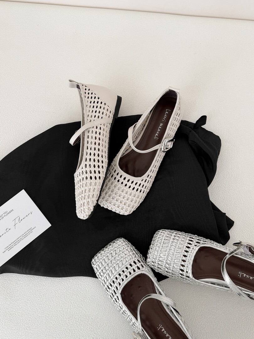 Pair of light woven Mary Jane flats displayed on a black fabric background