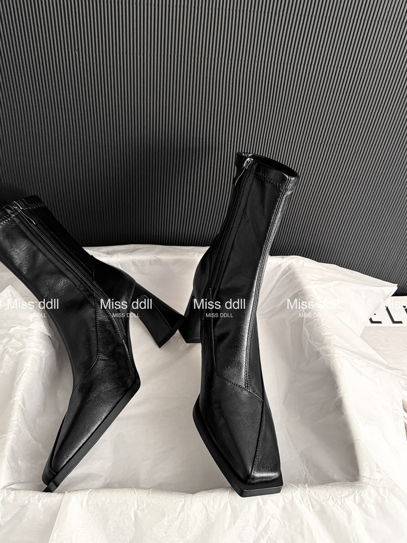 Black pointed-toe ankle boots with high heels displayed on tissue paper