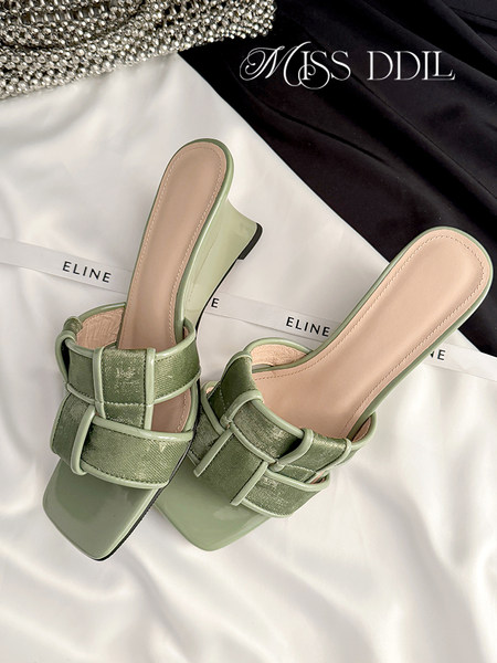 Pair of light green heeled slide sandals on a branded fabric background