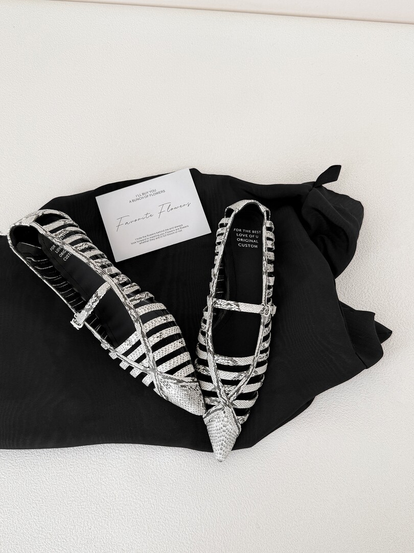 Pair of black and silver strappy sandals displayed on fabric with a small brand card