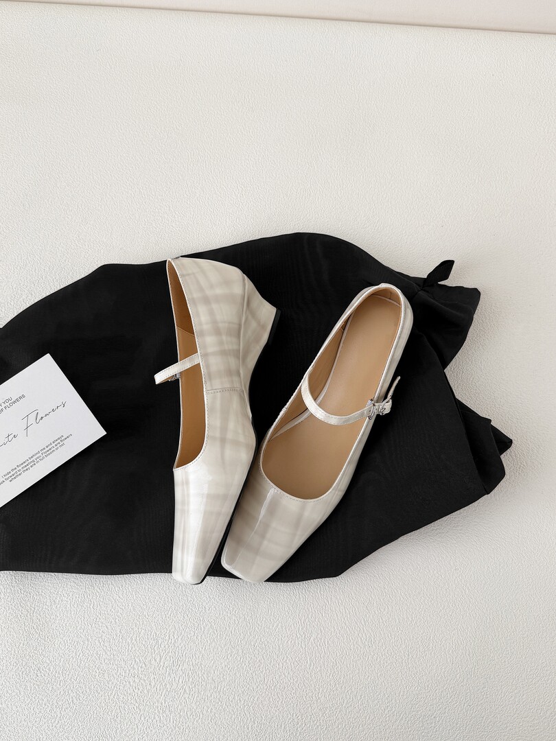 Pair of white pointed-toe Mary Jane flats displayed on a black fabric background