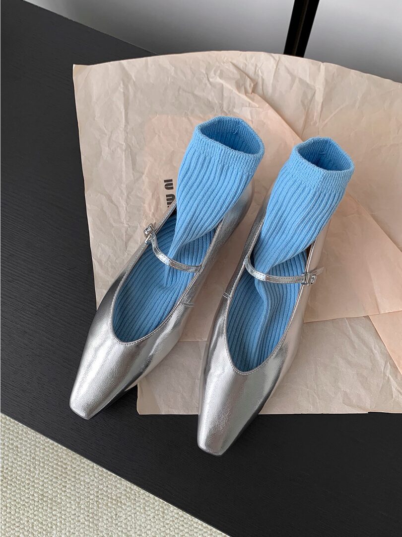 Pair of silver pointed-toe flats with blue ribbed socks displayed on paper