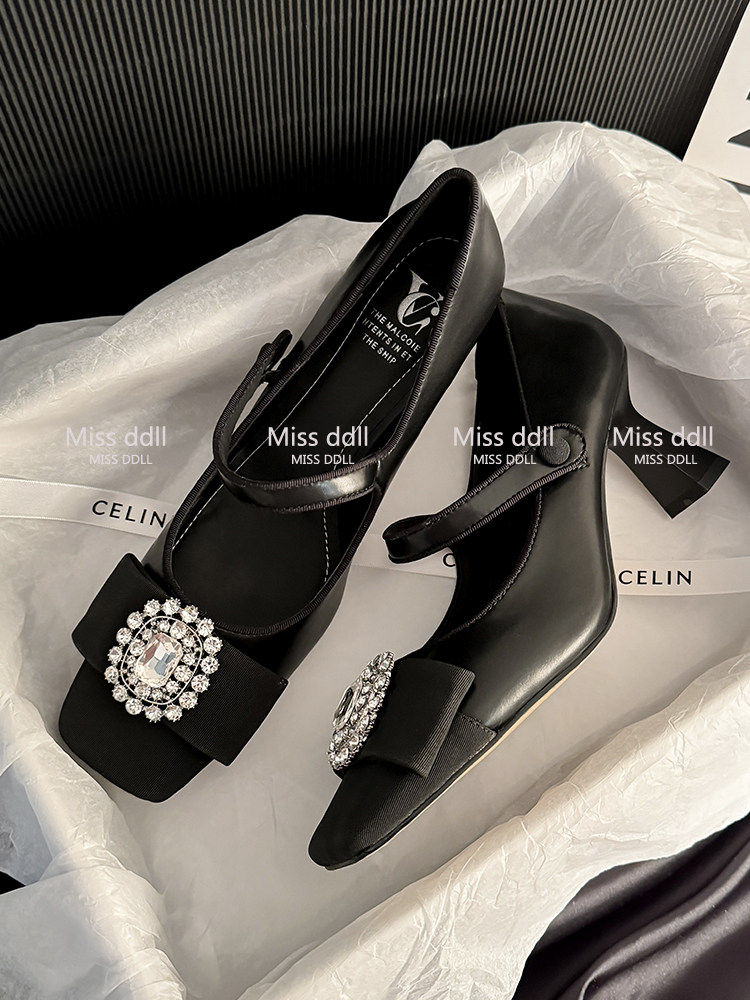 Black heeled sandals with jeweled embellishments displayed on branded packaging