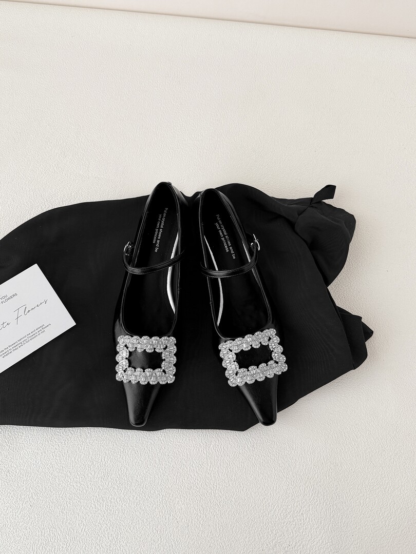 Black pointed-toe flats with jeweled buckle accents laid on black fabric