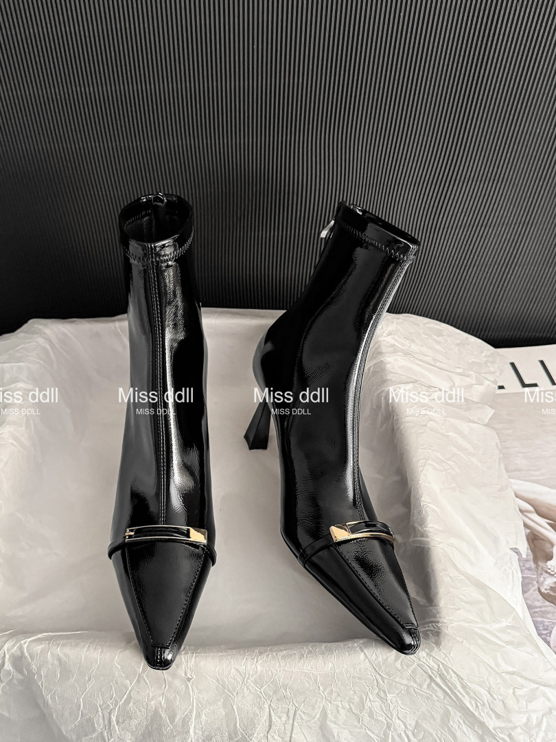Pair of black glossy pointed-toe high-heeled ankle boots displayed on a surface