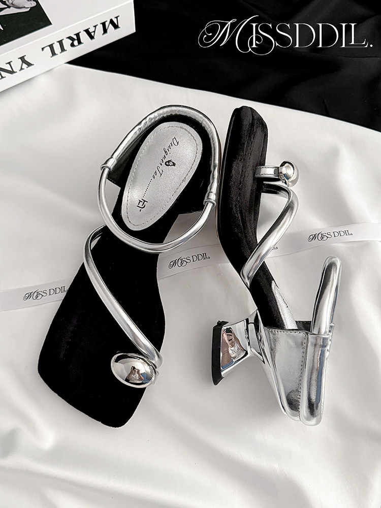 Silver strappy high-heeled sandals on a white and black background