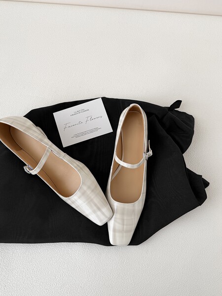 White Mary Jane flats displayed on a black fabric background with a small note card