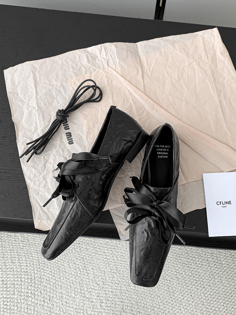 Black leather pointed-toe slip-on shoes with ribbon bows on paper packaging