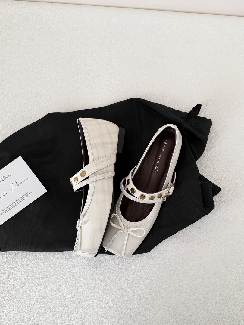 White Mary Jane flats with gold buckle details displayed on a black cloth background