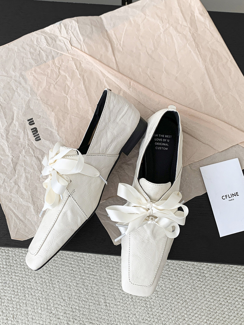 Pair of white low-heeled loafers with ribbon bows on a product display