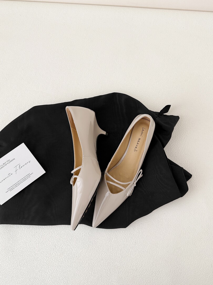 Pair of beige pointed-toe patent shoes laid on black fabric