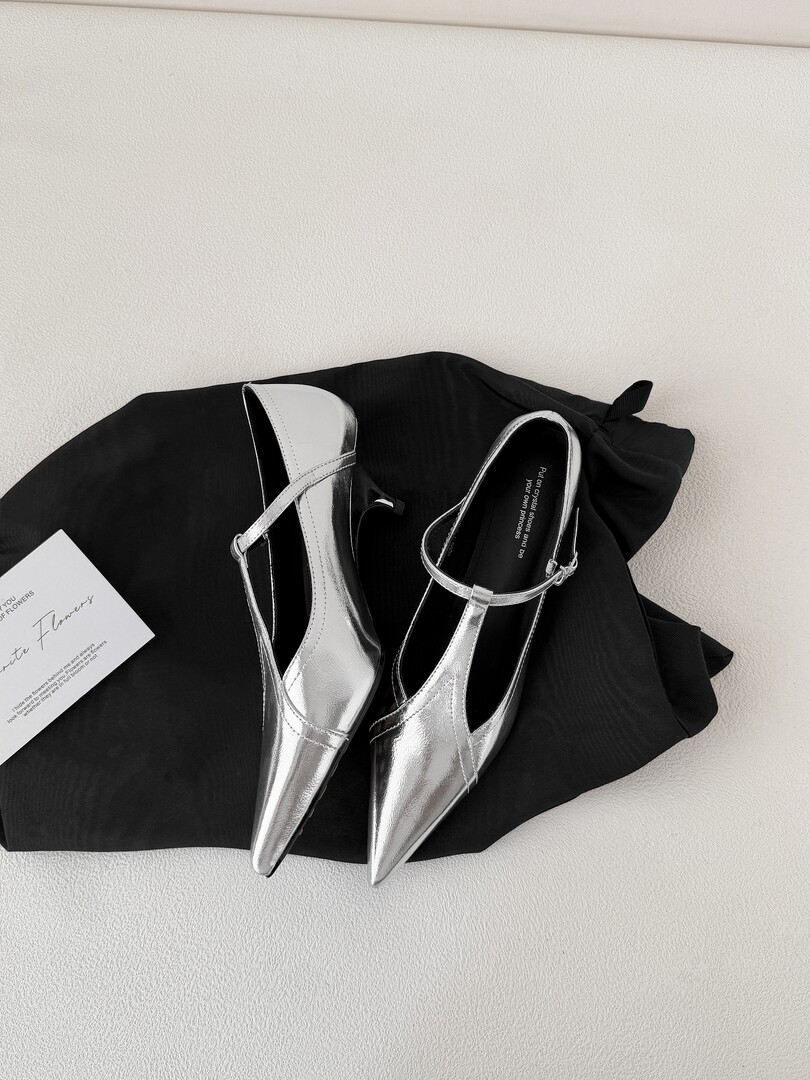 Silver pointed-toe slingback heels displayed on black fabric