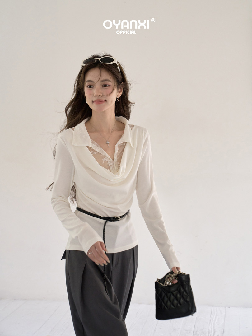 Model wearing a white draped long-sleeve blouse with dark trousers and a black handbag