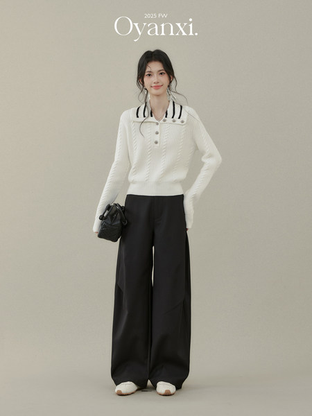 Model wearing a white knit sweater with black wide-leg pants and a black handbag