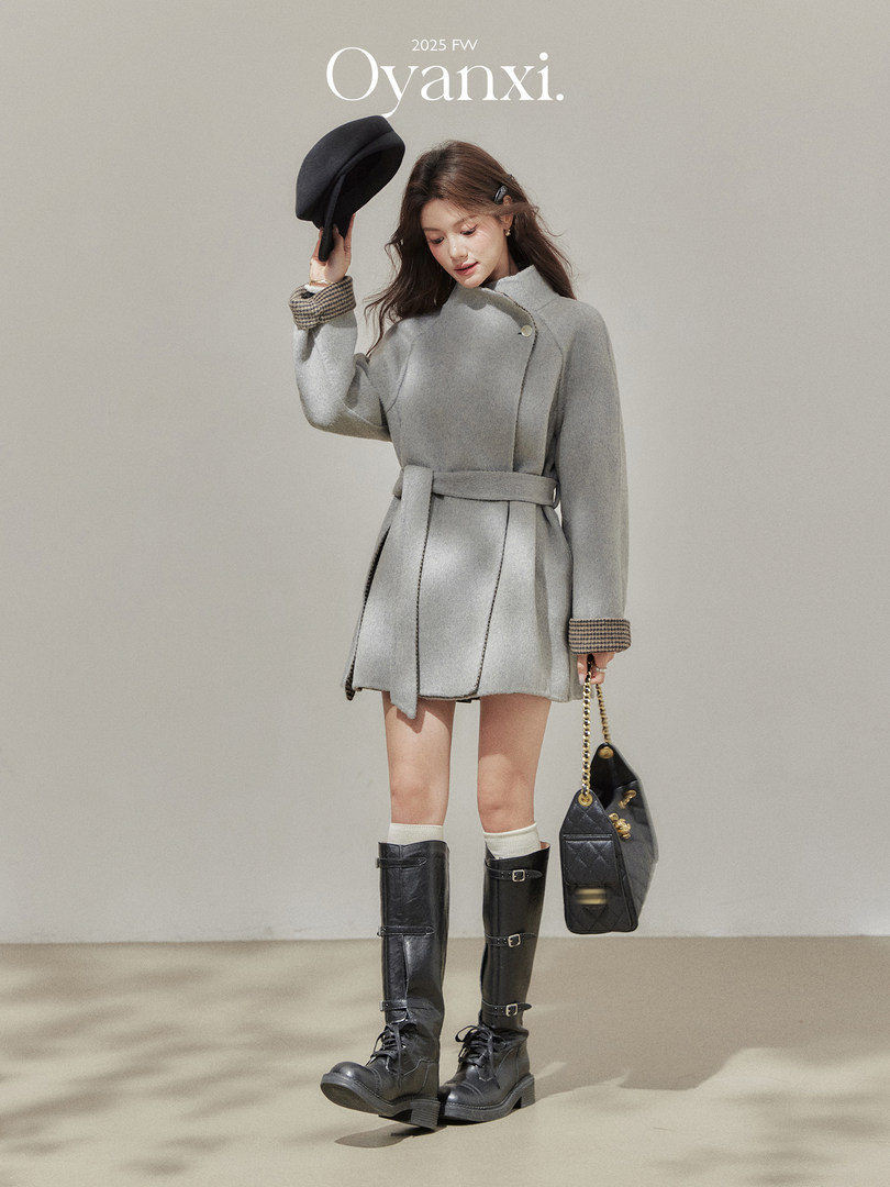 Model wearing a gray belted coat with black knee-high boots and a black handbag