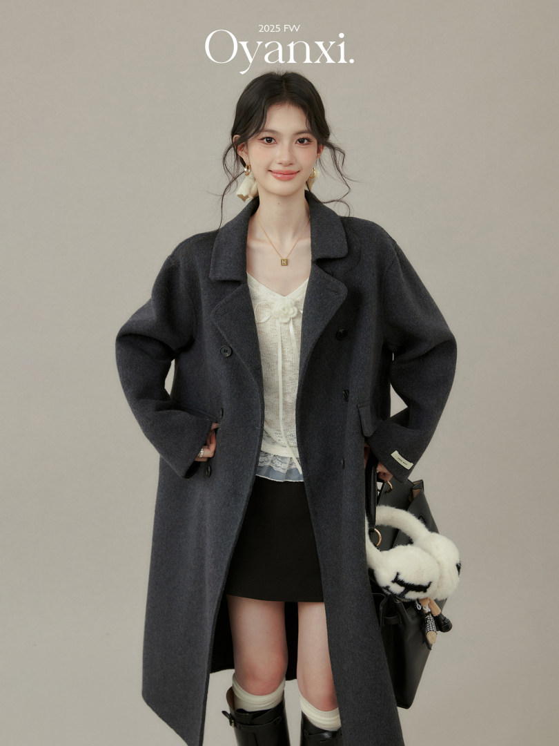 Woman wearing a dark gray long coat layered over a light top with a black mini skirt and handbag