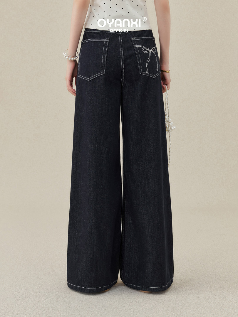 Model wearing dark wide-leg denim pants with contrast stitching and back pocket details