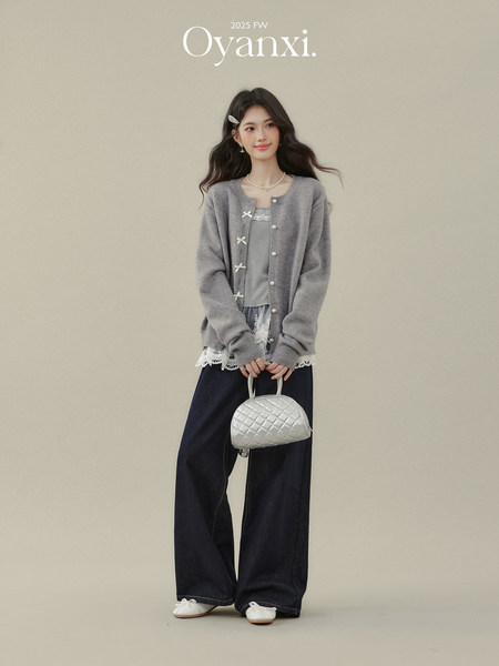 Model wearing a gray cardigan and wide-leg pants while holding a white quilted handbag