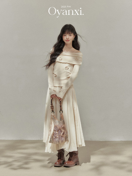 Model wearing a cream off-shoulder dress with brown boots and a handbag