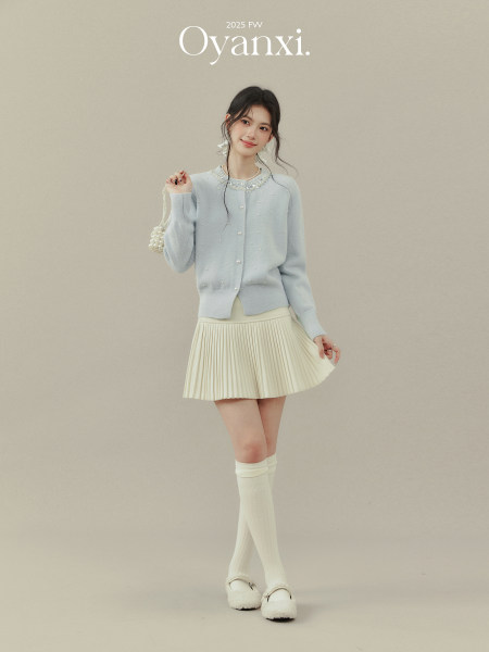 Model wearing a light blue embellished cardigan with a cream pleated mini skirt and knee socks