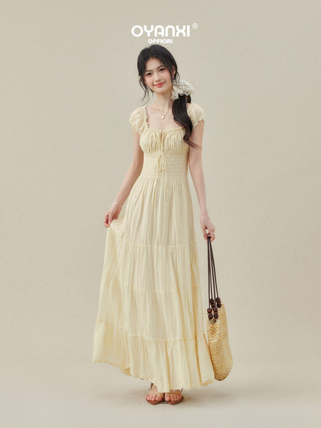 Model wearing a cream tiered maxi dress with a straw bag