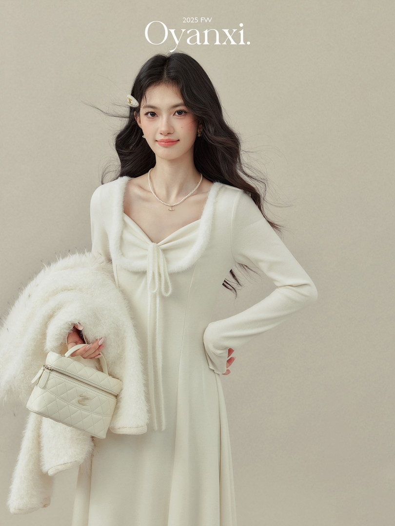 Model wearing an ivory long-sleeve dress and holding a quilted handbag