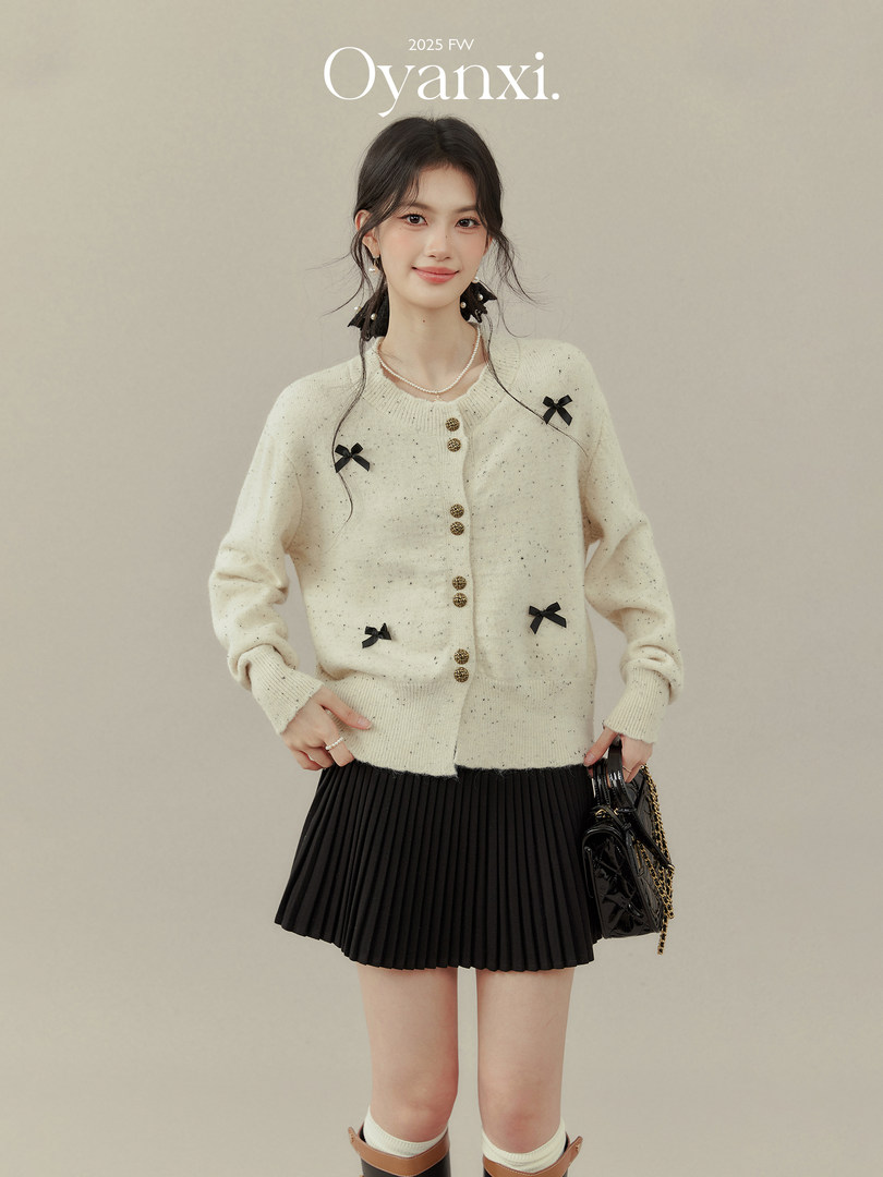Model wearing a cream speckled cardigan with black bows and a black pleated skirt