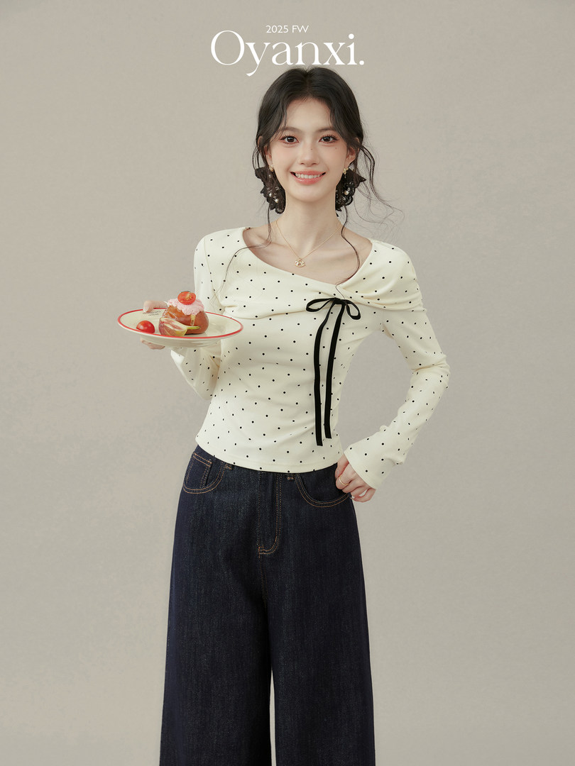 Model wearing a white polka dot long-sleeve top with dark wide-leg jeans