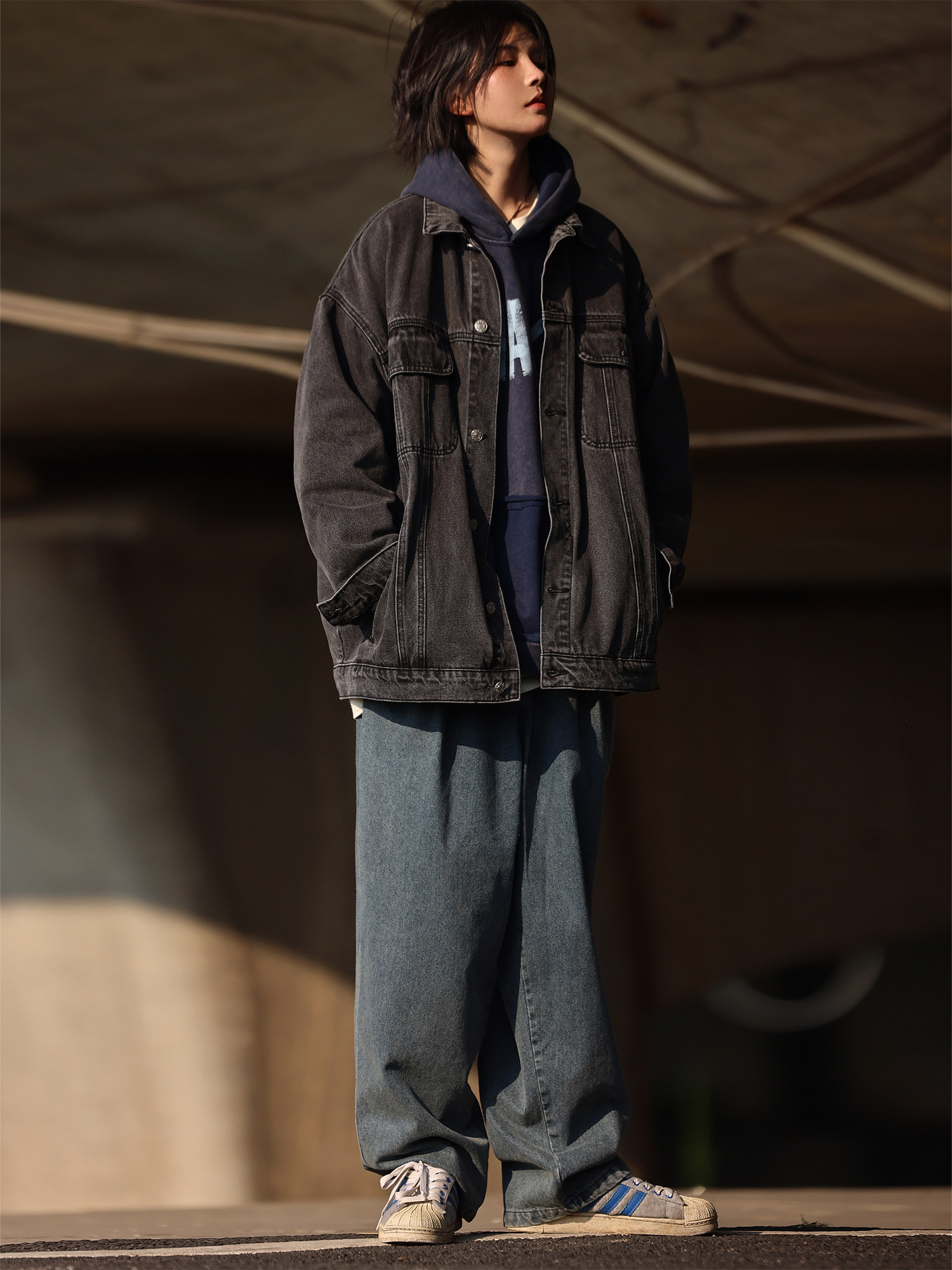 Oversized washed black denim jacket layered over a hoodie with loose trousers