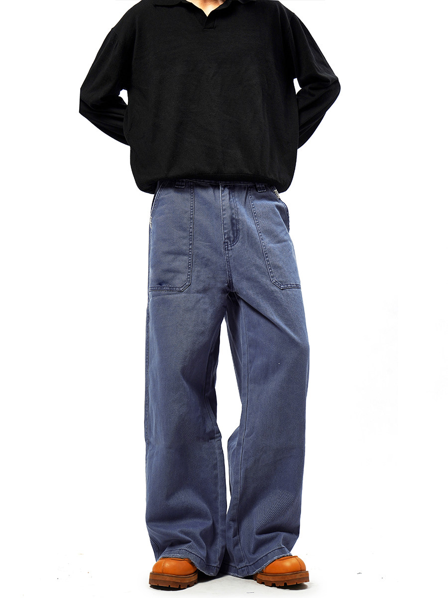 Person with hands behind back, wearing a black long-sleeve shirt, EastLyst French Workwear Pants with a distressed finish, and orange-brown shoes against a plain white background. Face is not visible.