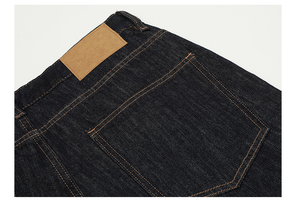 Close-up of the back pocket and waistband of EastLyst Vintage Jeans in dark blue raw denim, highlighted by orange stitching and a blank brown leather patch on the waistband.