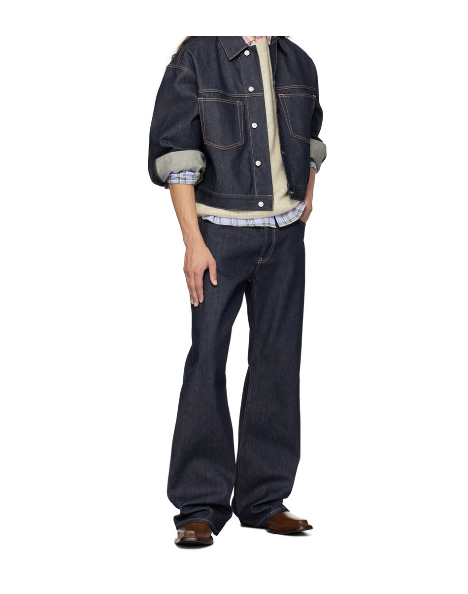 A person wearing EastLyst's Vintage Jeans, paired with a dark premium raw denim jacket, shirt, sweater, and brown shoes stands with hands at their sides. Their face is not visible.