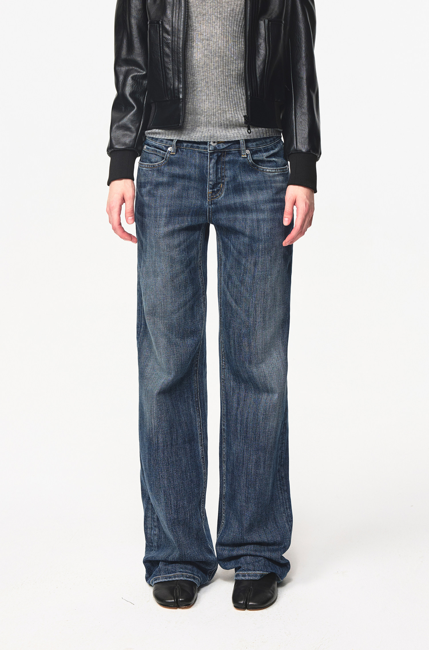 A person wearing a gray ribbed top, black leather jacket, EastLyst Slub Textured Casual Pants in vintage indigo wash, and black shoes stands against a plain white background. The image is cropped at the shoulders.