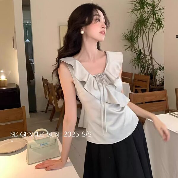 Woman modeling a light gray ruffled sleeveless blouse with a black skirt in a cafe setting