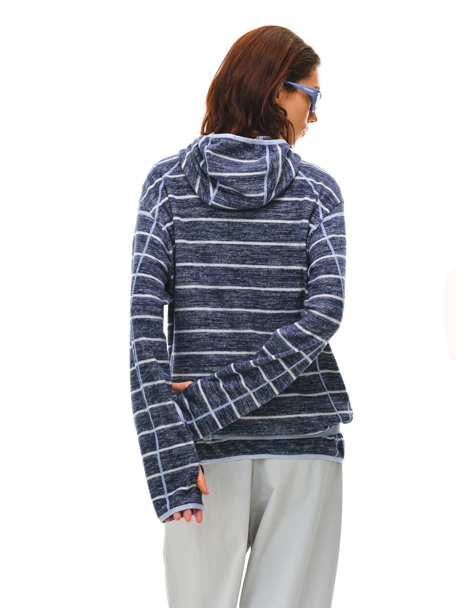 A person with shoulder-length brown hair and blue sunglasses wears the EastLyst Textured Stripe Knit Hoodie and light pants, standing with their back to a white background.