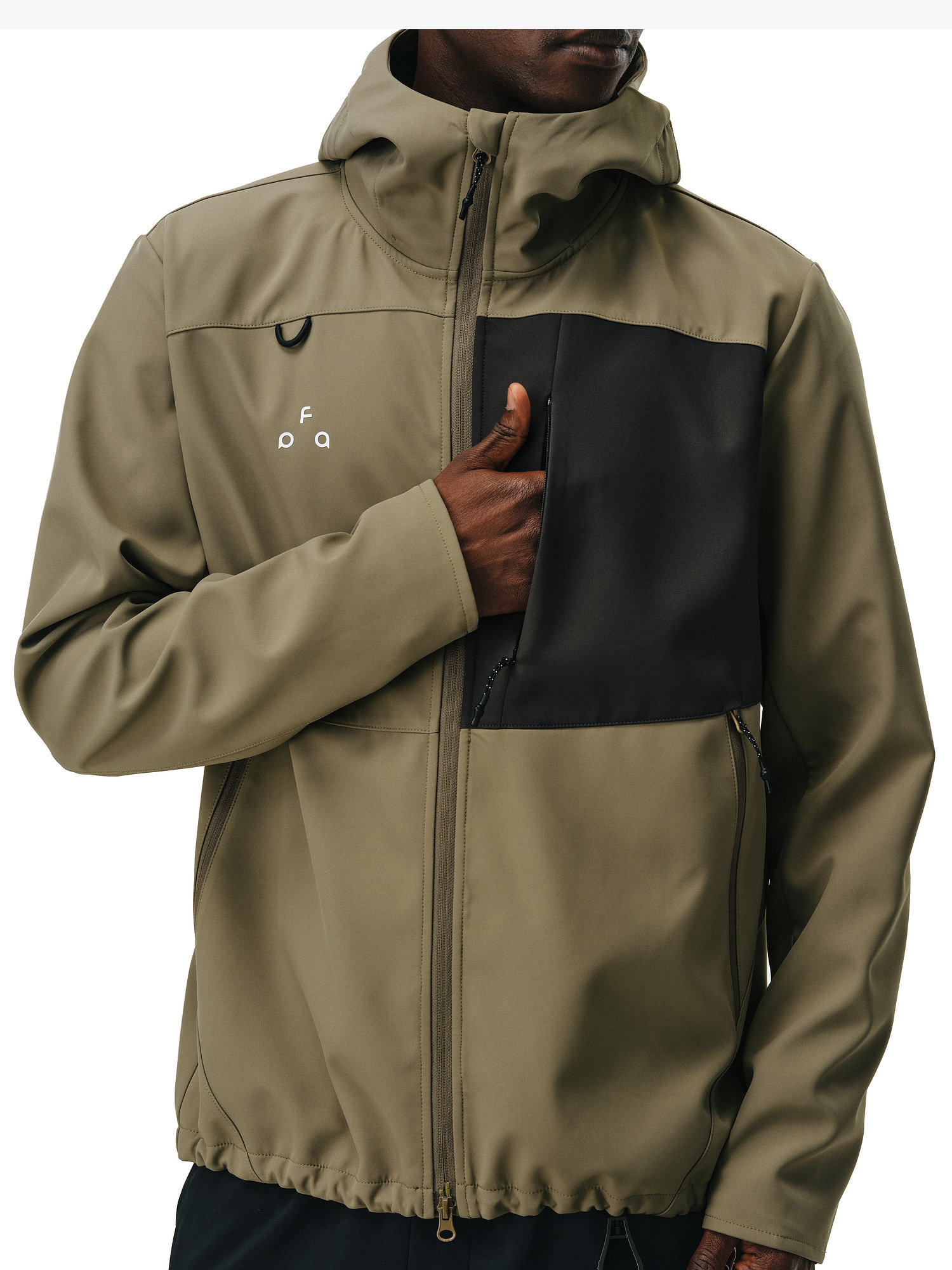A person, shown from the shoulders down, wears the EastLyst Color-Block Water-Resistant Softshell Jacket in olive green with a black chest pocket and white logo, holding it closed. The jacket features a front zipper and drawstring hem.
