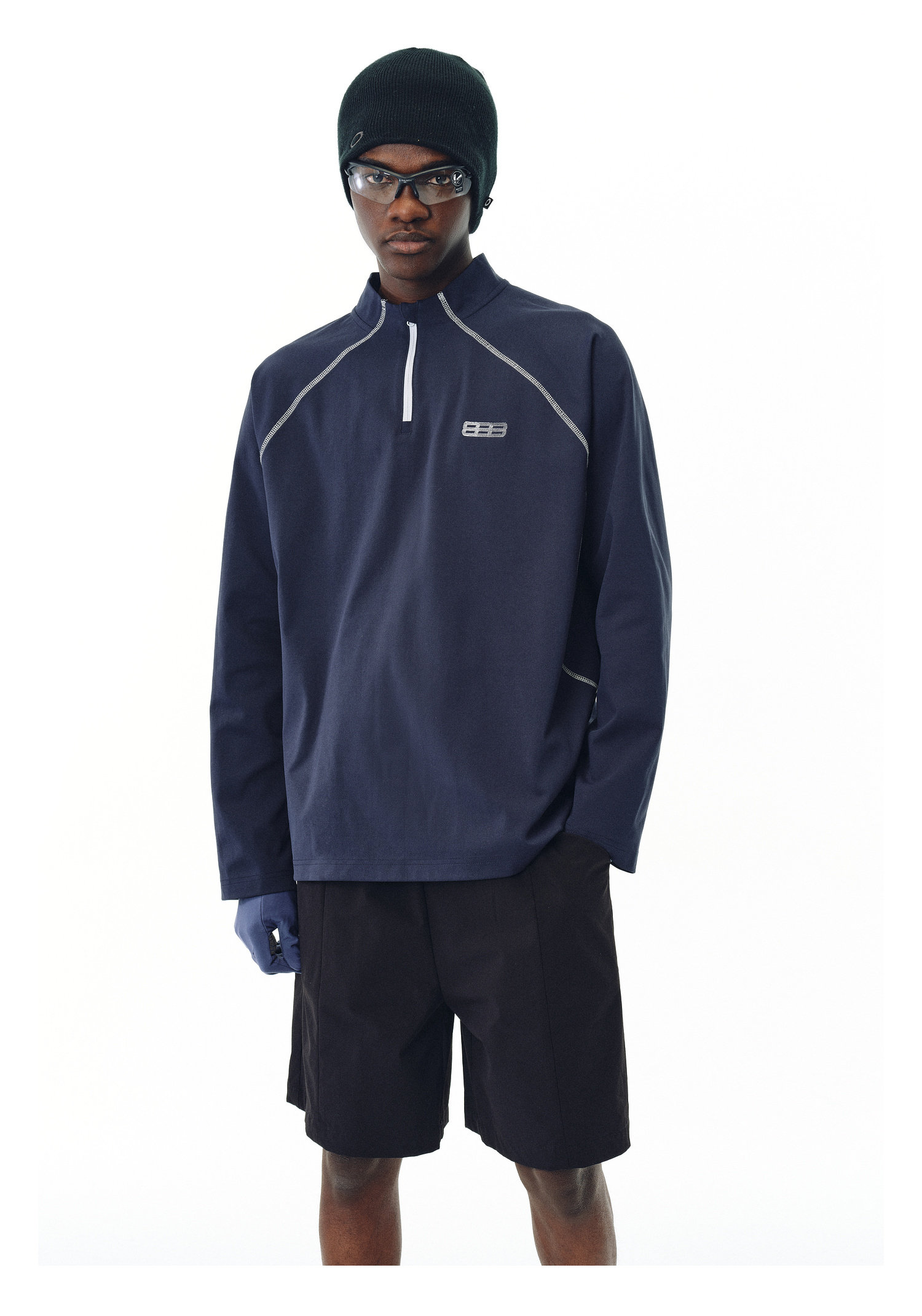 A person wearing the EastLyst Premium Anti-Pilling Hemp Long Sleeve Tee in navy, paired with black shorts, a black beanie, dark sunglasses, and a blue glove, stands against a plain white background.