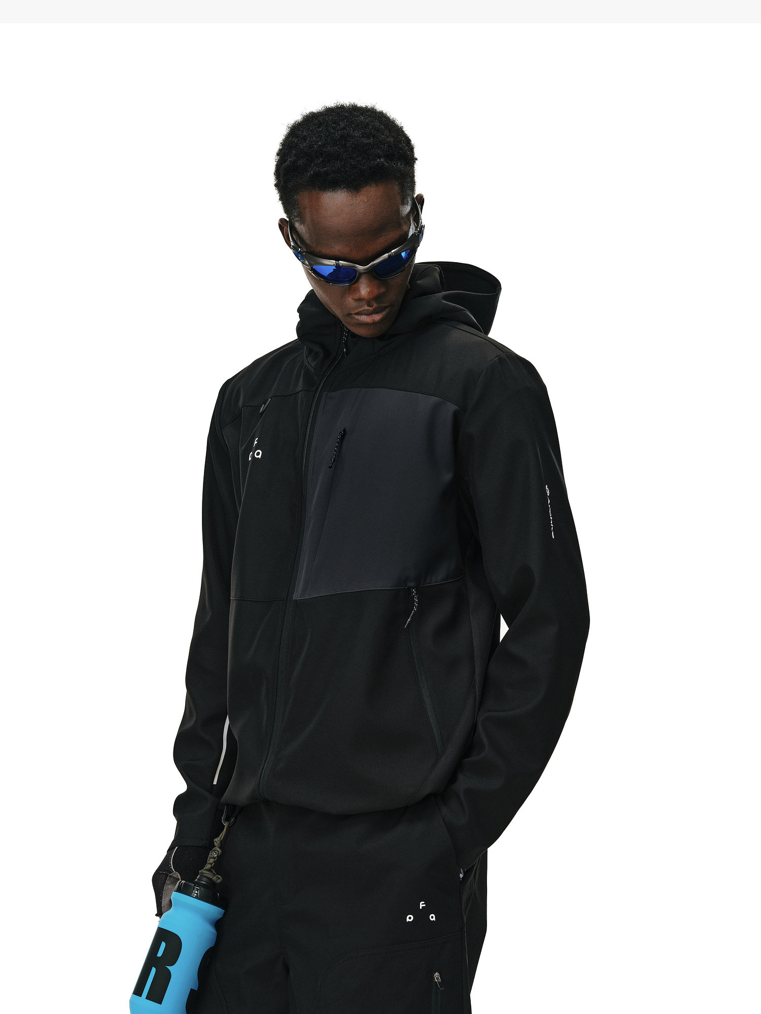 A man wears the EastLyst Color-Block Water-Resistant Softshell Jacket and dark pants, holding a blue water bottle and wearing reflective sunglasses against a white background.