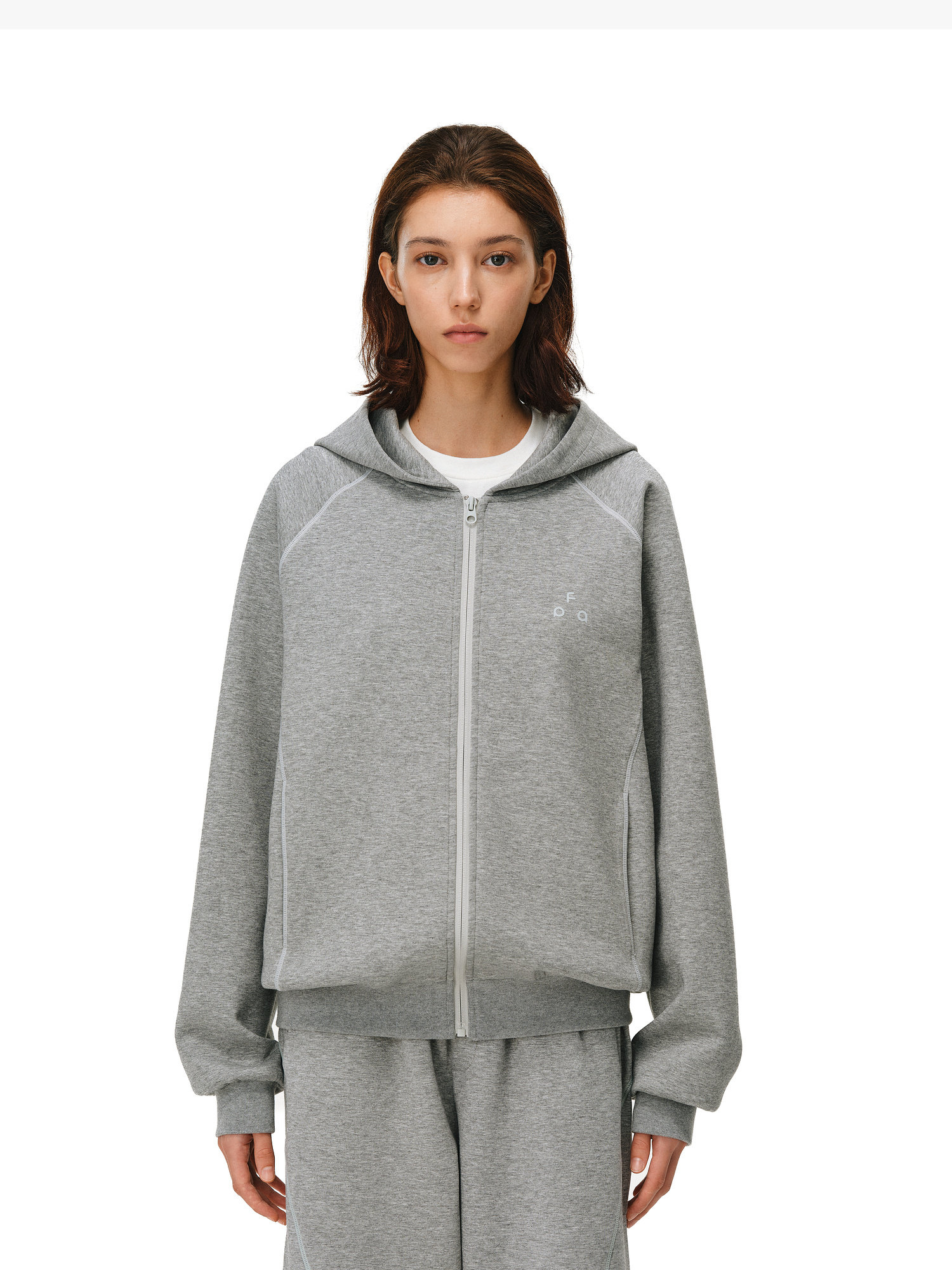 A person with medium-length brown hair wears the EastLyst Constant Warmth Zip Hoodie in light gray with matching sweatpants, crafted from premium fabric. They stand against a plain white background facing forward with a neutral expression.