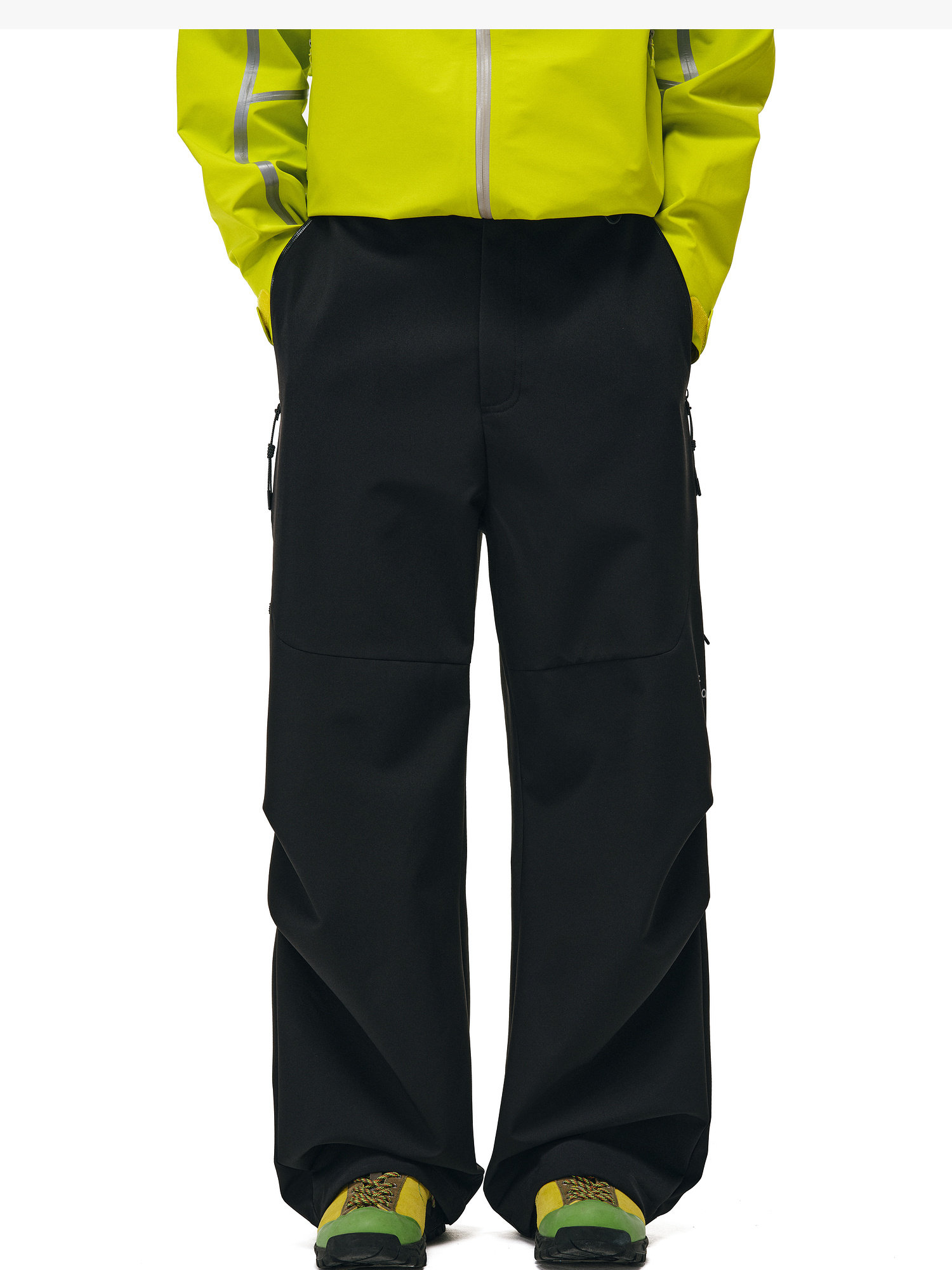 Wearing EastLyst Softshell Joggers, a bright yellow moisture-wicking jacket, and green patterned sneakers, the person stands with hands in pockets against a white background.