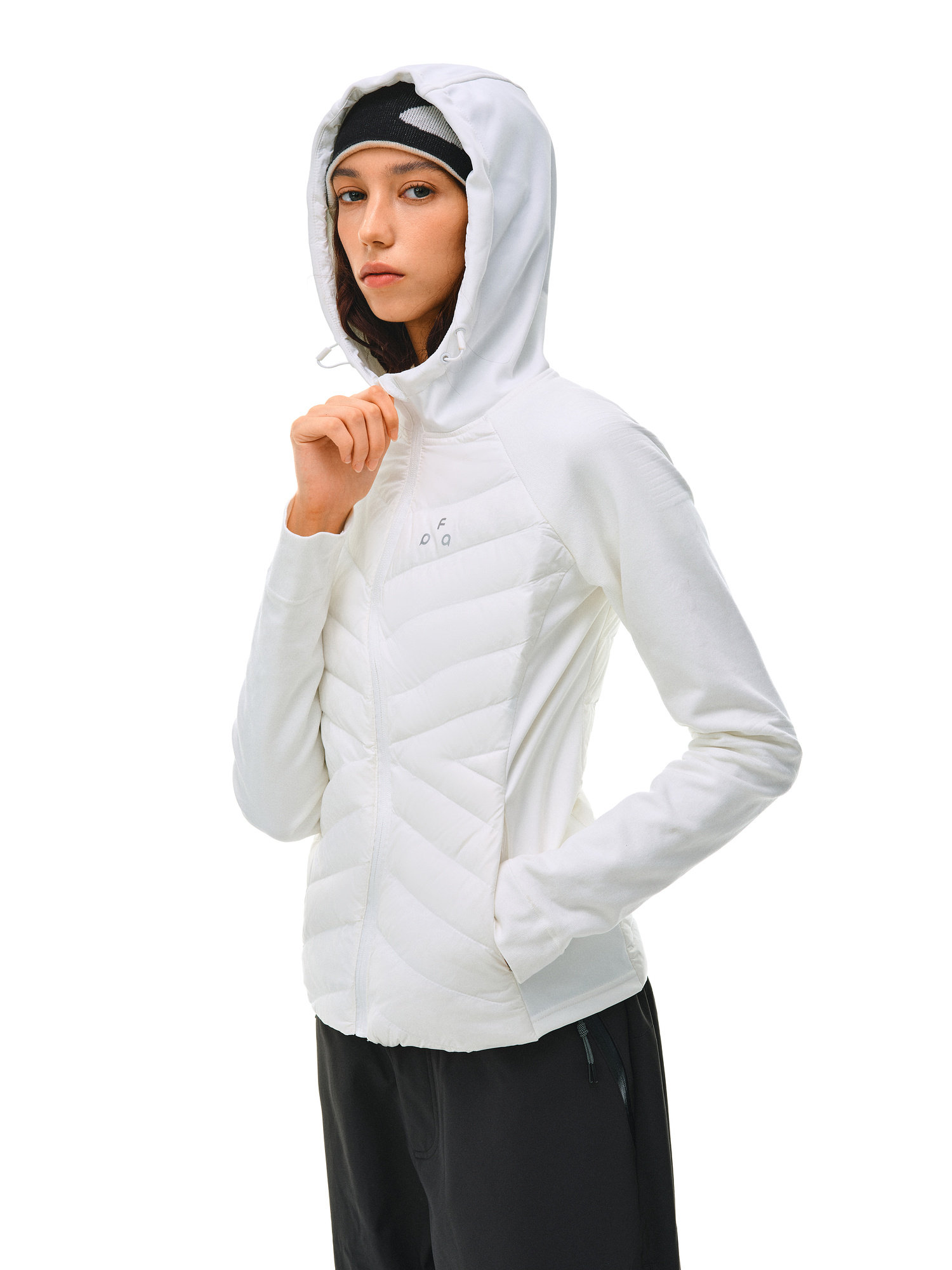 A woman models the EastLyst Quilted Hooded Down Jacket in white with black pants, touching her hood. She wears a black headband and stands against a plain white background, facing slightly sideways with a neutral expression.